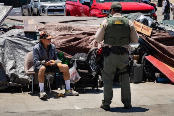 A deputy from the Los Angeles Sheriff's Department speaks to a homeless man sitting in front of his encampment in the Venice area of Los Angeles on June 8, 2021. (John Fredricks/The Epoch Times)
