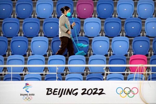 A maintenance worker walks through an empty section of spectator stands near a logo for the Beijing 2022 Winter Olympics at the National Speed Skating Oval in Beijing on Oct. 10, 2021. (Mark Schiefelbein/AP Photo)