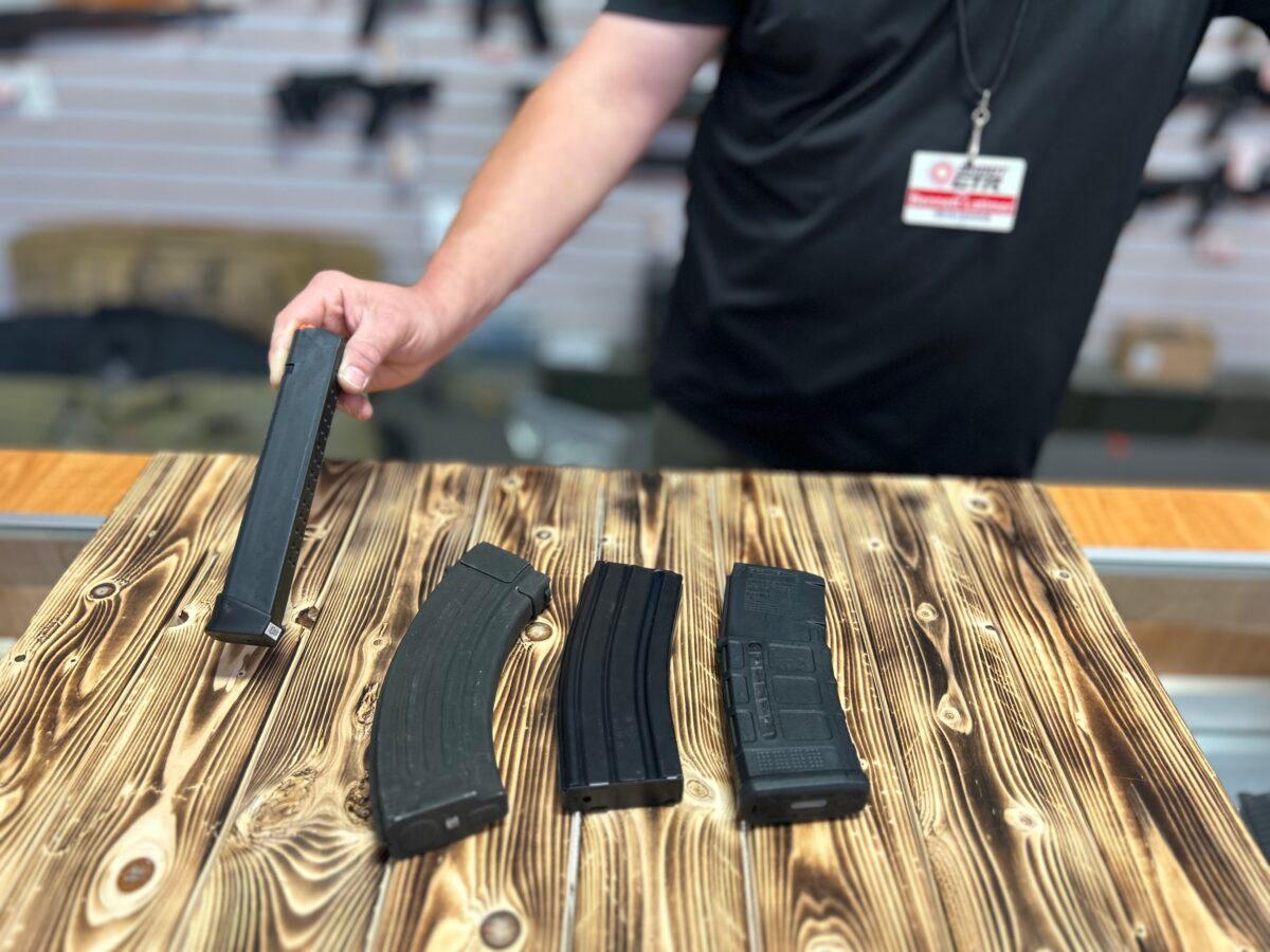 A gun store employee shows the differences between (L–R) high-capacity magazines for a handgun, an AK-style rifle, and AR-style rifles at Lawful Defense in Gainesville, Fla., on April 19, 2023. (Nanette Holt/The Epoch Times)