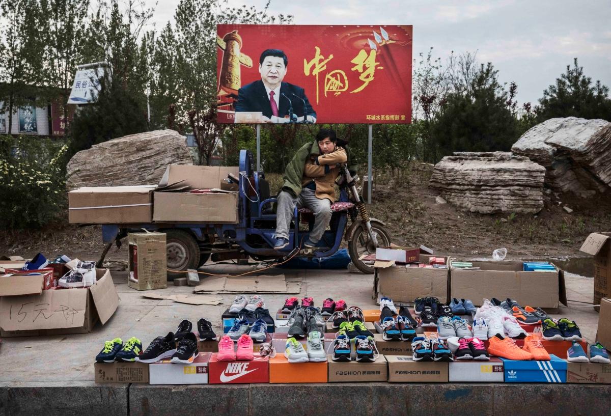 A Chinese vendor sells sneakers and shoes in the street in front of a sign showing Chinese leader Xi Jinping with "China Dream" written on it, in Shijiazhuang, Hebei Province, China, on April 9, 2017. (Kevin Frayer/Getty Images)