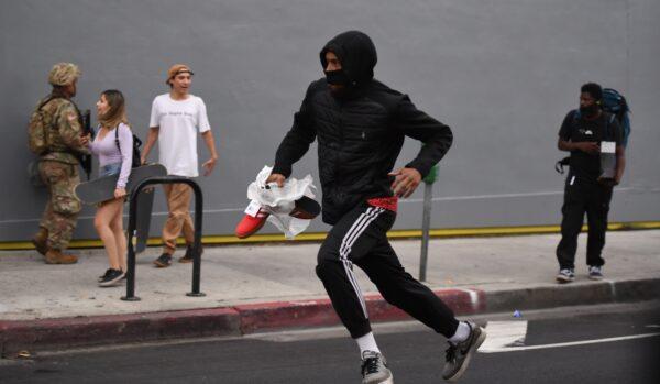A suspected looter carrying a pair of shoes run past National Guard soldiers in Hollywood, Calif., on June 1, 2020, after a demonstration over the death of George Floyd. (Robyn Beck/AFP via Getty Images)